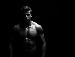 Black and white studio shot of a strong unrecognizable young handsome male athlete posing shirtless on black background copyspace bodybuilder man with muscular body fitness sports willpower concept.
