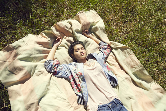 Young woman lying on blanket listening music with headphones