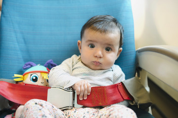 Baby girl sitting on a plane seat with a doll and the seat belt fastened