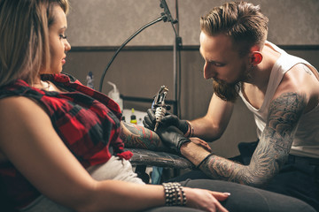 Serene man making tattoo on woman hand