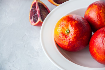 Fresh ripe whole and slices of blood oranges in a plate on a white stone background. Copy space and close up.
