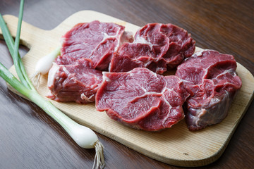 Raw beef slices on a cutting board with a spring onion
