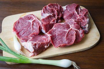 Raw beef slices on a cutting board with a spring onion