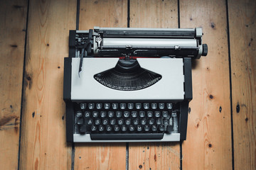 Vintage gray typewriter on the wooden floor. Black buttons white letters