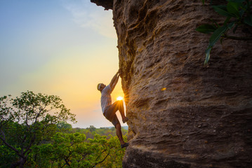 man climbing on the rock at sunset in background