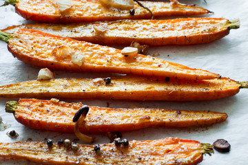 Roasted spring carrots on parchment with garlic, pepper peas and coriander on baking sheet. Selective focus
