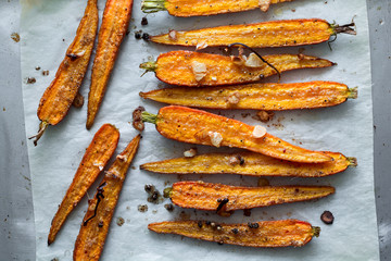 Roasted spring carrots on parchment with garlic, pepper peas and coriander on baking sheet. Selective focus