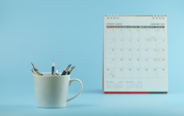 pencils in white cup with calendar on blue background