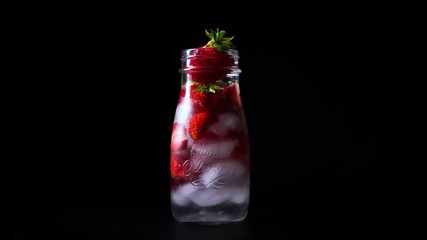 infused water with strawberry and ice on a rotating black tray and black background.