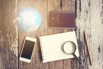 magnifying glass, globe, passport, smartphone and blank notebook on wooden table. Top view travel concept.