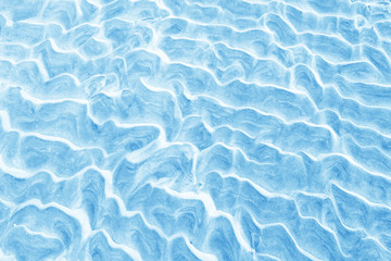 Fototapeta premium Natural ocean beach sand texture background. Wet sand background with wavy pattern after the tide in light blue color. Close up horizontal composition.