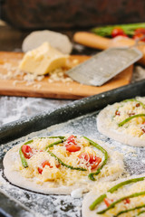 Cooking process of making mini pizza - small and personal, with cheese, tomatoes and asparagus.