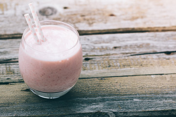 Strawberry pink smoothie in a glass with a straw on a old wooden rustic table. Toned image. Summer and healthy lifestyle concept.