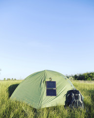 The tent stands in a clearing in the woods solar panel hangs on the tent.