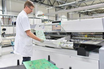Arbeiter an einer Maschine zur Bestückung von Platinen mit Elektronik - Herstellung von Hitech...