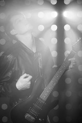 Naklejka premium Black and white photo of young rock musician playing electric guitar and singing. Rock star on background of spotlights