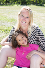 blonde mother sitting in a park with the long-haired brunette girl