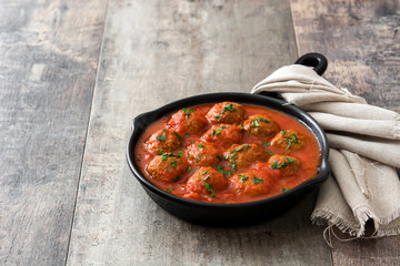 Meatballs with tomato sauce in iron frying pan on wooden table