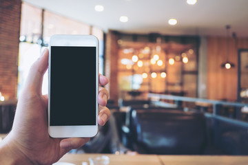 Mockup image of hand holding white mobile phone with blank black screen in modern loft cafe