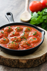Meatballs with tomato sauce in iron frying pan on wooden table