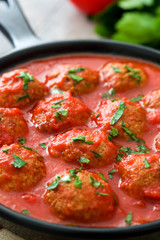 Meatballs with tomato sauce in iron frying pan on wooden table