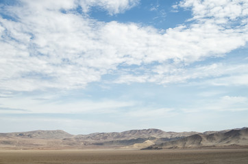 Fototapeta na wymiar Arid lands of the desert under blue cloudy sky