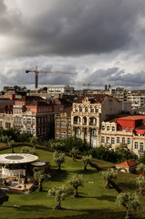 Zielony park na pierwszym planie, w tle budynki, dzwig. Zachmurzone, burzowe niebo. Pionowe ujęcie. Porto miasto w Portugalii. 