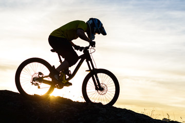 Fototapeta na wymiar Silhouette of Cyclist Riding Down the Mountain Bike on Rocky Hill at Sunset. Extreme Sport Concept.