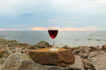 A glass of red wine standing on a rock against the background of the sea