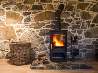 The interior of a cosy, stone cottage with stone walls and a fireplace with logs burning in a wood...
