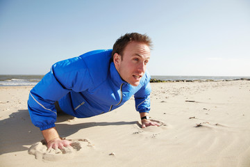 Young man doing push ups on sandy beach