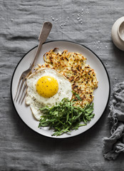 Potato latkes, fried egg and arugula - delicious healthy breakfast or snack. On a gray table, top view