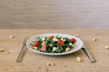 fresh salad with tomato, feta cheese, arugula, cashew on the wooden table