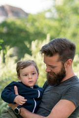 Young hipster father holding his little son in park