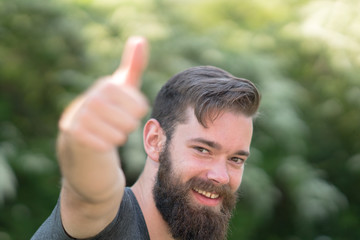 Handsome smiling guy with beard man doing thumbs up gesture. Selective focus on his face on background