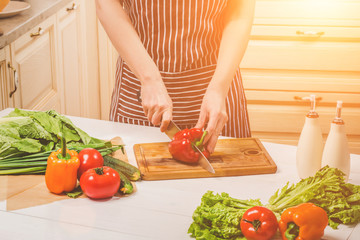 Young woman cooking in the kitchen at home. A woman cuts a pepper and vegetables with a knife.