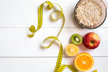 Fitness concept with fruit, bowl of oatmeal and centimeter. Top view background concept.