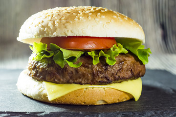 Delicious hamburger with cheese, lettuce and tomato on a stone