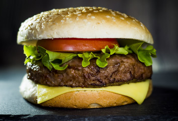 Delicious hamburger with cheese, lettuce and tomato on a stone