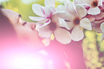 girl smelling pink, blossoming, magnolia flowers from tree