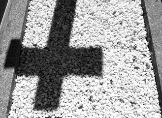 The shadow of a cross on a floor of little white stones in a cemetery: concept of sorrow and grief. Black and white.