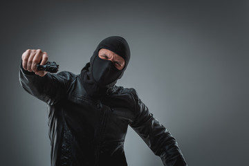 Masked robber with gun, looking into the camera.