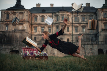 Woman sorceress reads book and flies in air against backdrop of ancient castle. Levitation.