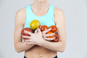 the sports woman holding a lot of apples in the hands on the grey background