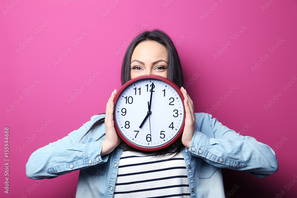 Wall mural young woman holding a clock on pink background