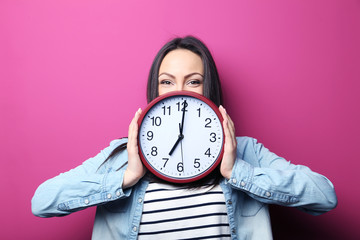 Young woman holding a clock on pink background