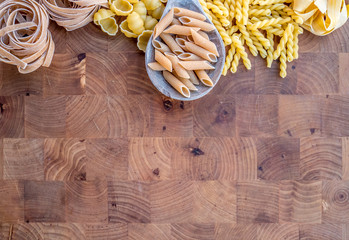Various mix of dry pasta on wooden rustic background and a wooden spoon. Top view.