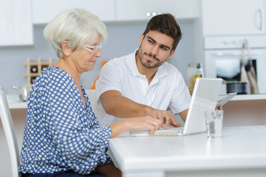 Young man showing elderly lady how to use laptop