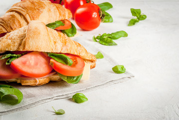 Light and hearty spring breakfast. Croissant with ham, cheese, fresh tomatoes and basil. On a white stone table, with the ingredients. Copy space