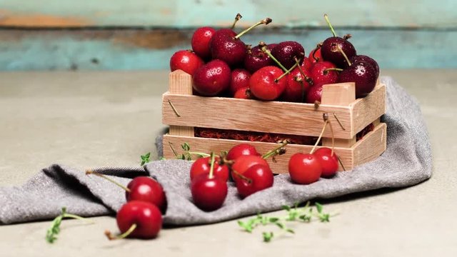 Red ripe cherries in small wooden box on kitchen countertop. Rotating slide.